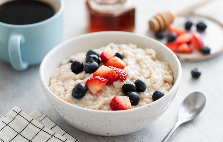 Bowl of oatmeal with fruit, coffee and honey in background