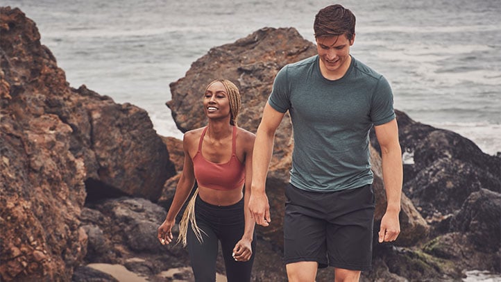 Two people in athletic clothes walking outside by the ocean