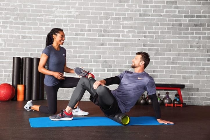 Female NASM trainer assisting male client with foam roller stretch on glutes