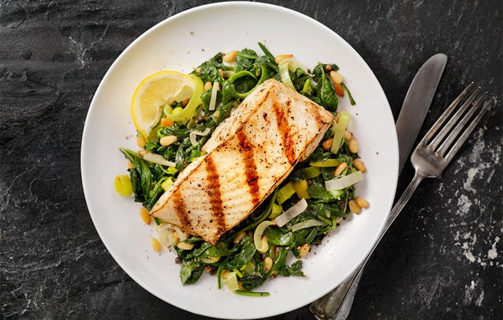 Grilled fish (protein) on a bed of mixed greens
