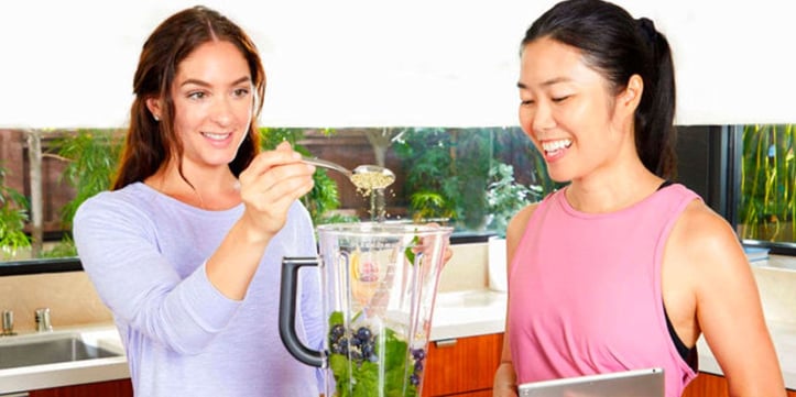 Two women making a healthy smoothie in kitchen