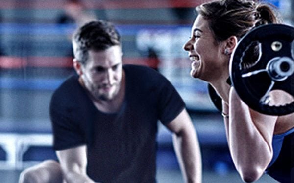 Trainer assisting female client with barbell back squat