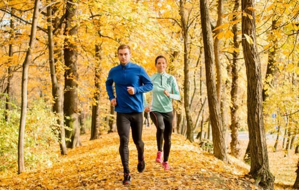 Man and woman running outside around fall leaves