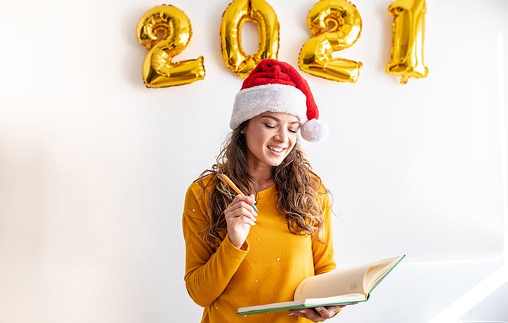 woman writing her new years resolutions for 2021 wearing a Christmas hat