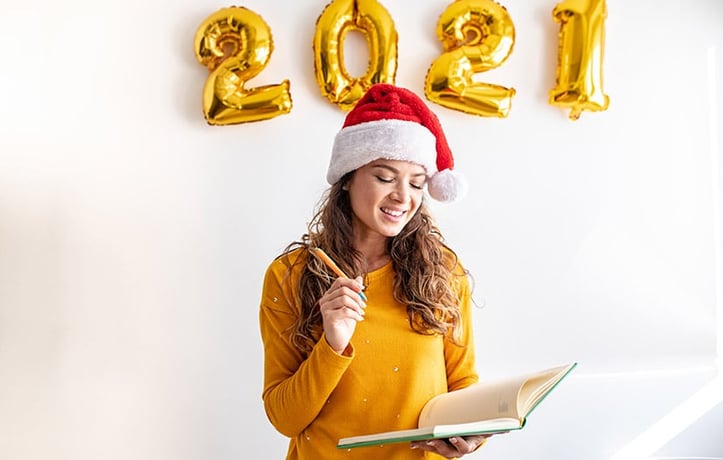 woman writing her new years resolutions for 2021 wearing a Christmas hat