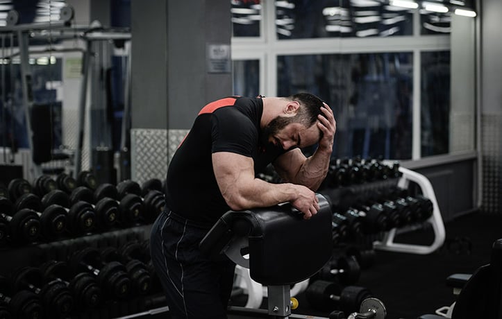 Male leaning on preacher curl bench with hand on head