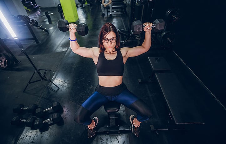 Woman doing seated dumbbell shoulder press inside gym
